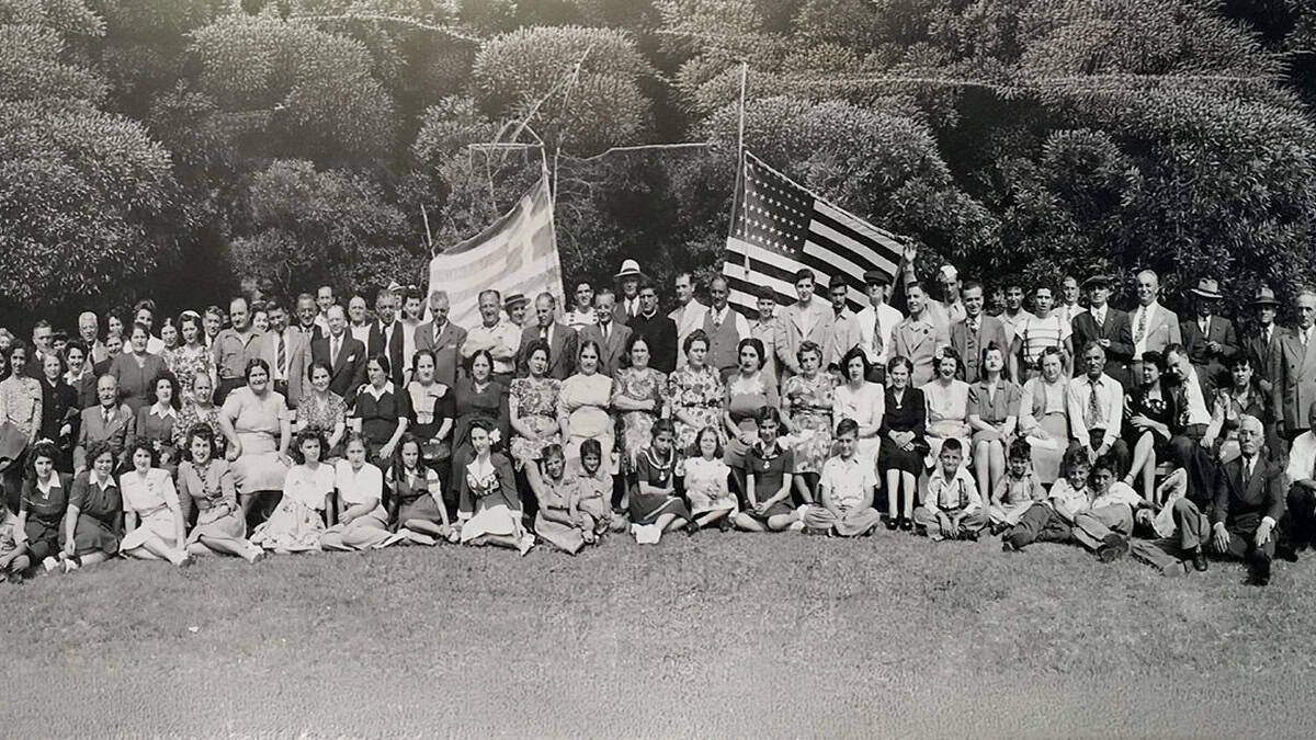 Group of early Greek immigrants in the United States gathered with Greek and American flags