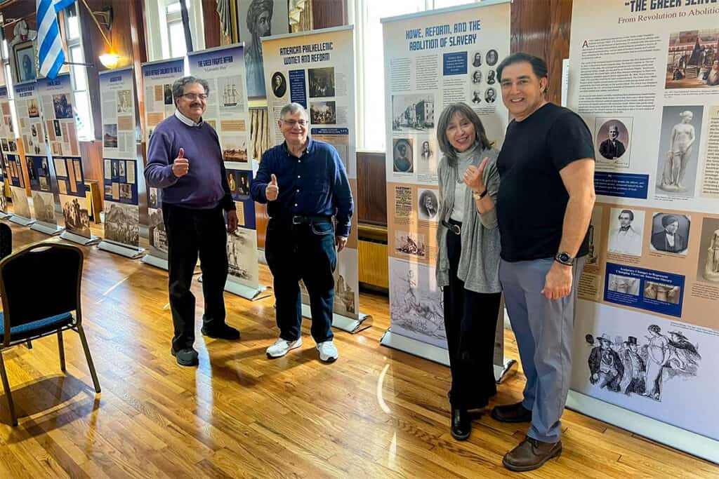 People standing in front of exhibition panels at “The Greek Revolution Through American Eyes” at the Stathakion Cultural Center in Astoria