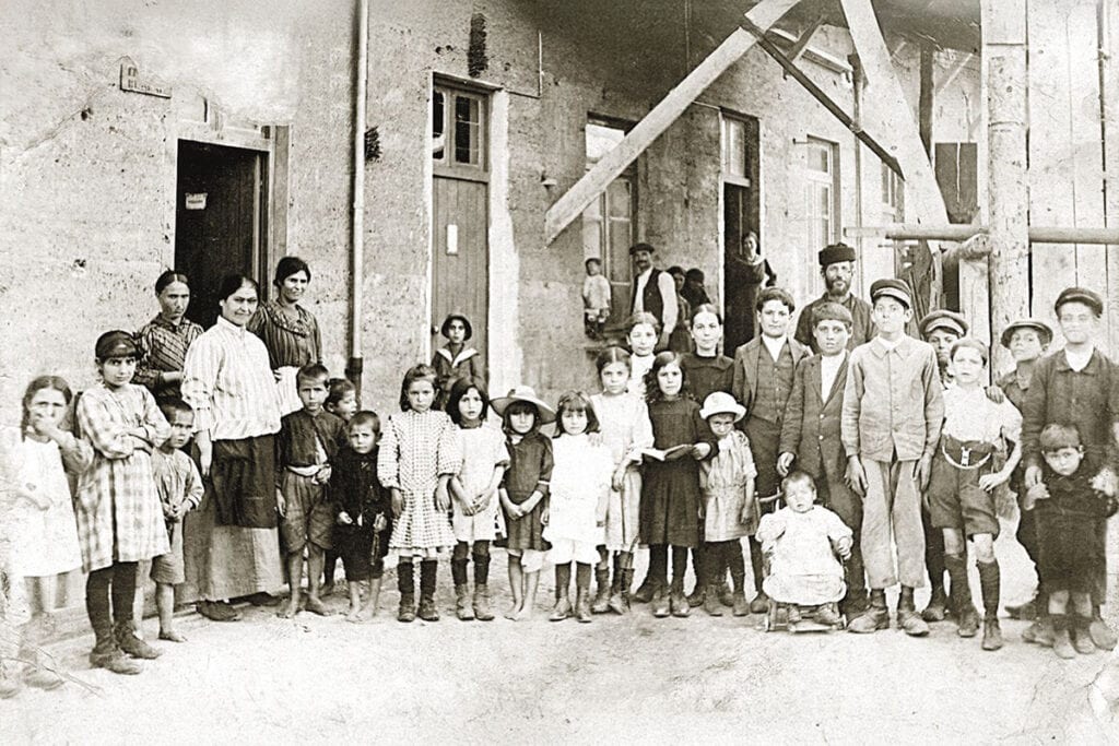 Children and adults gathered outside a building in Volos, Greece, reflecting family life shaped by poverty and migration.