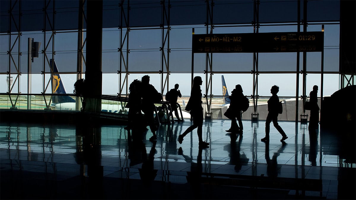 Silhouettes of travelers walking through an airport terminal