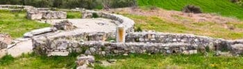 Excavation area at Amphipolis with stone remains, green fields, and hills in the background.