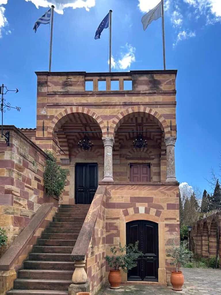 The Argentikon mansion in Kambos, Chios, with red-stone arches, exterior stairs, and flags above the entrance