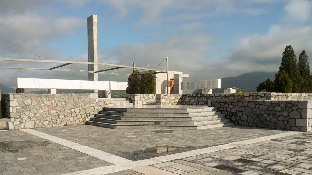 Memorial site above Distomo with stone paving, marble structures, and mountains in the background.