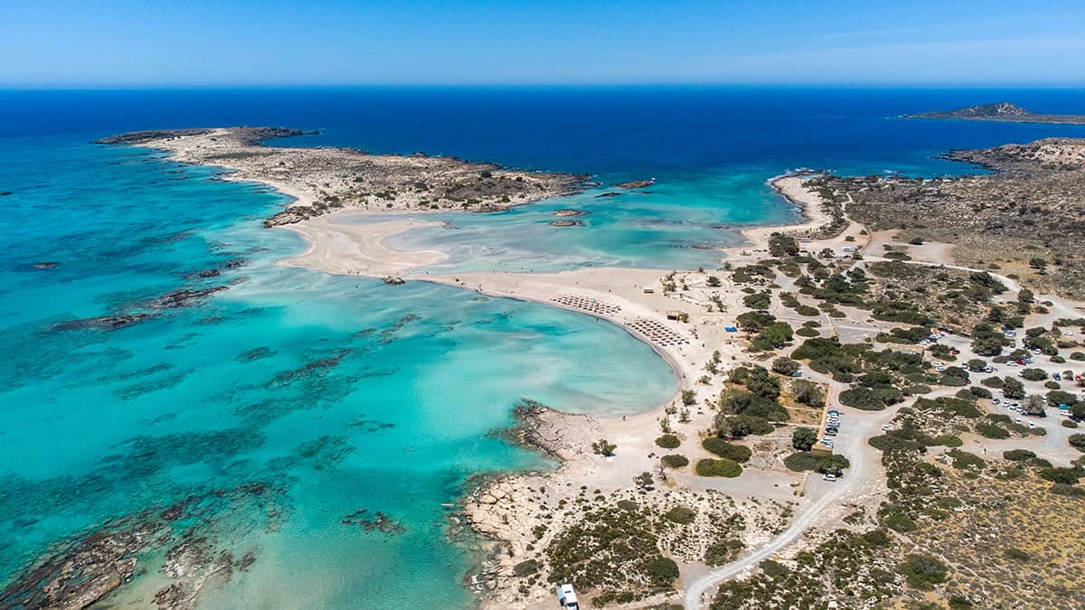 Aerial view of Elafonisi beach in Crete with turquoise water, sandbars, coastal vegetation, and beach access roads