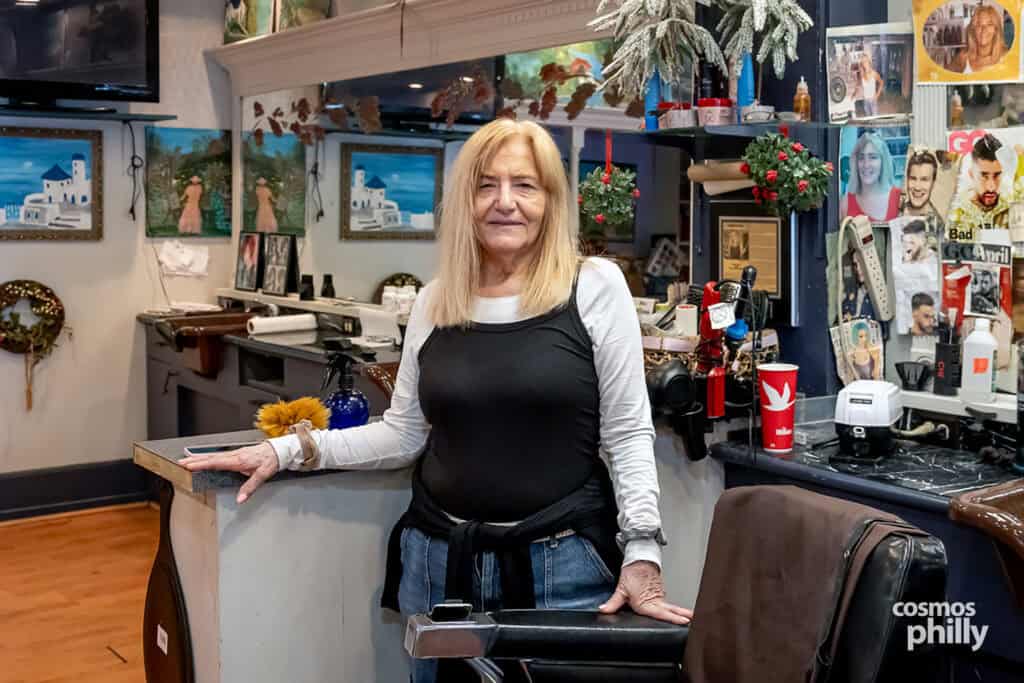 Giota Hartas standing beside a barber chair inside her longtime barbershop in Media, Pennsylvania.