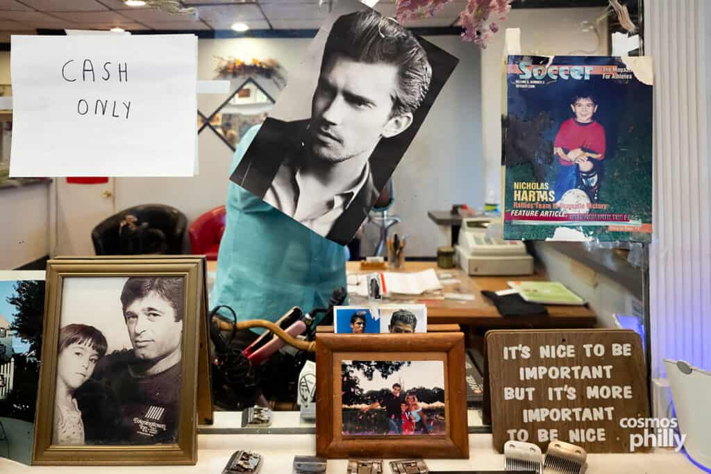 A cash-only sign, family photos, clippers, and keepsakes displayed on the mirror inside Giota’s Barbershop.
