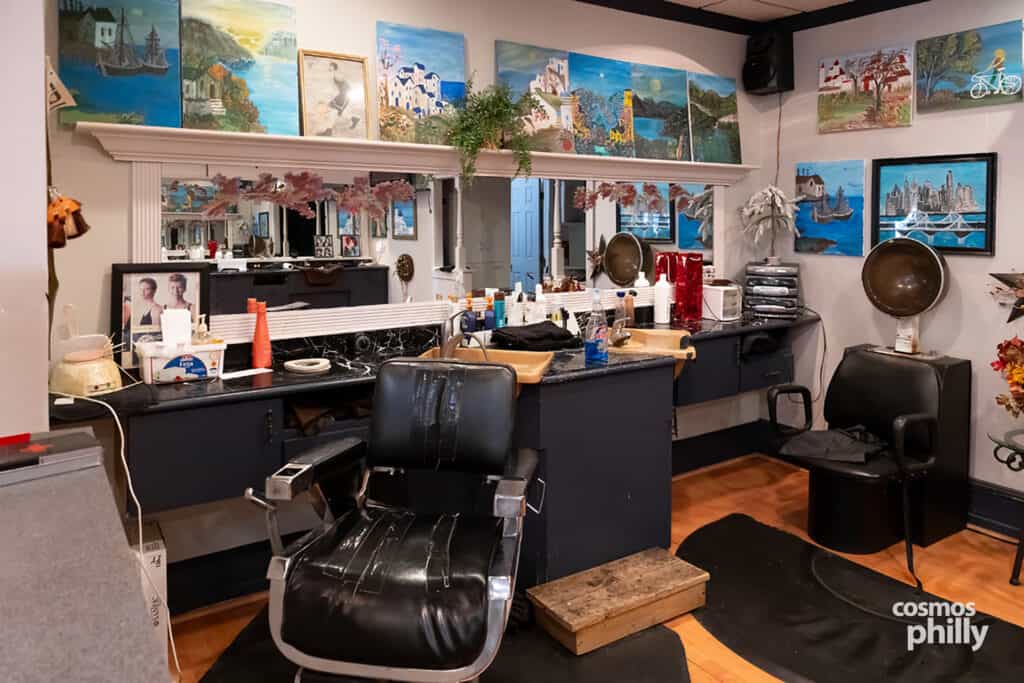 A black barber chair inside Giota’s Barbershop, surrounded by mirrors, hair products, and Giota’s paintings.