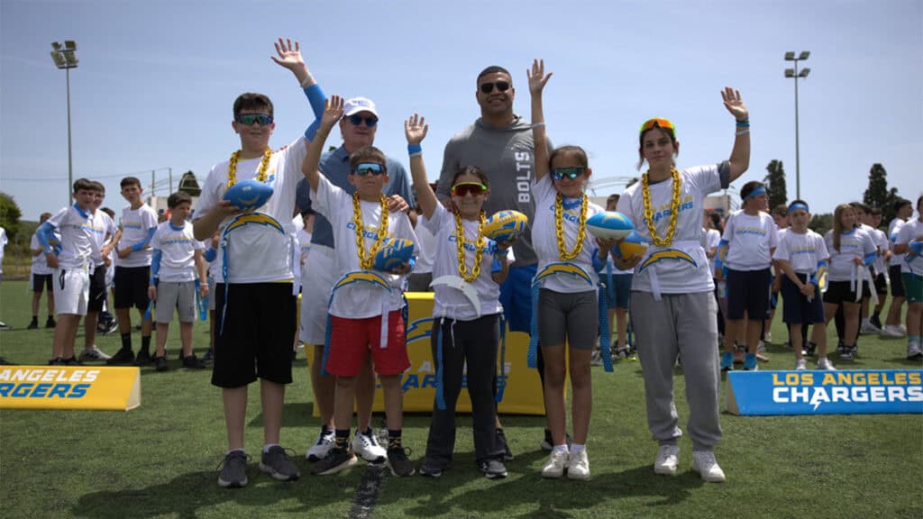 Dean Spanos and Shawne Merriman standing with winners from the NFL Flag Football Camp in Methoni.
