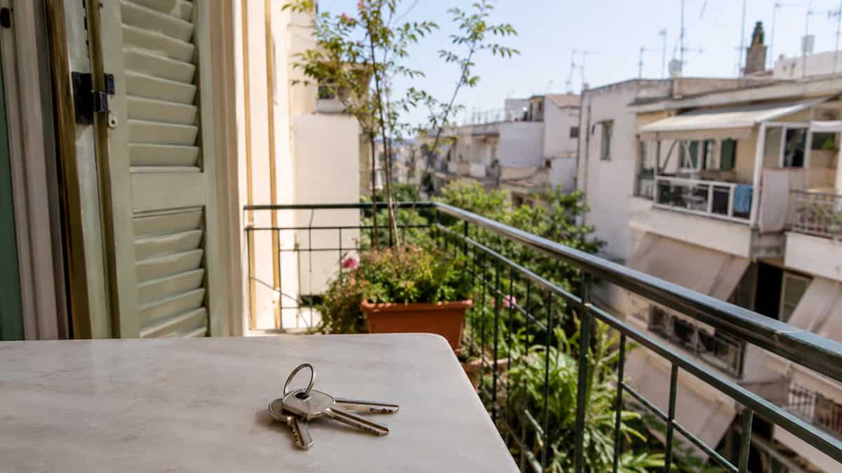 House keys on a balcony table overlooking a Greek apartment neighborhood,