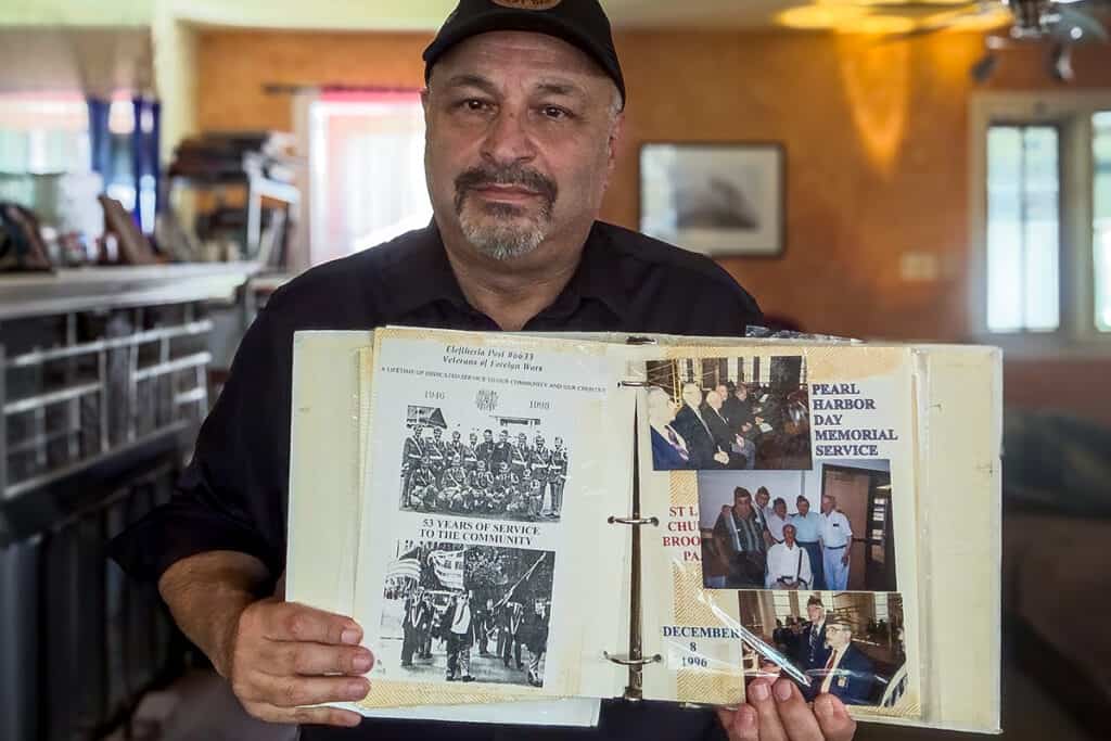 A GAHSP representative holds an open Eleftheria VFW Post 6633 album with historic photographs and clippings.