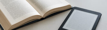 Open book beside an unbranded e-reader on a desk