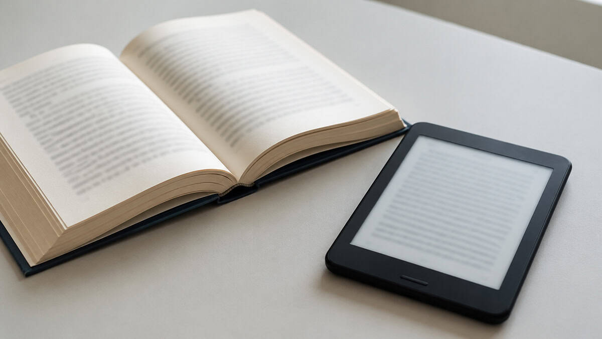 Open book beside an unbranded e-reader on a desk