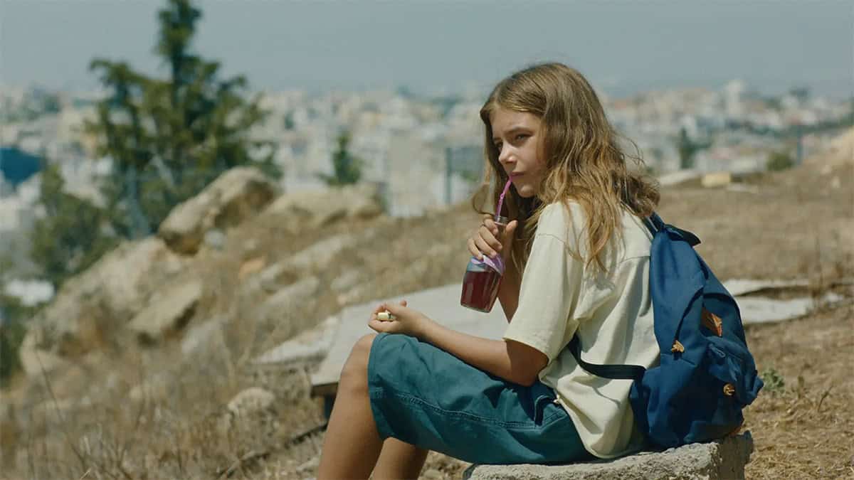 Young girl with a backpack drinks from a bottle on a dry hillside in a scene from Hold Onto Me.