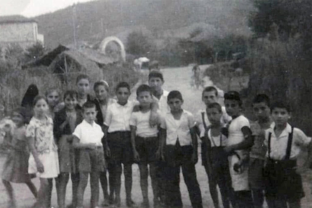 Archival black-and-white family photograph from Drama, Greece, showing children standing together on a village road in 1953