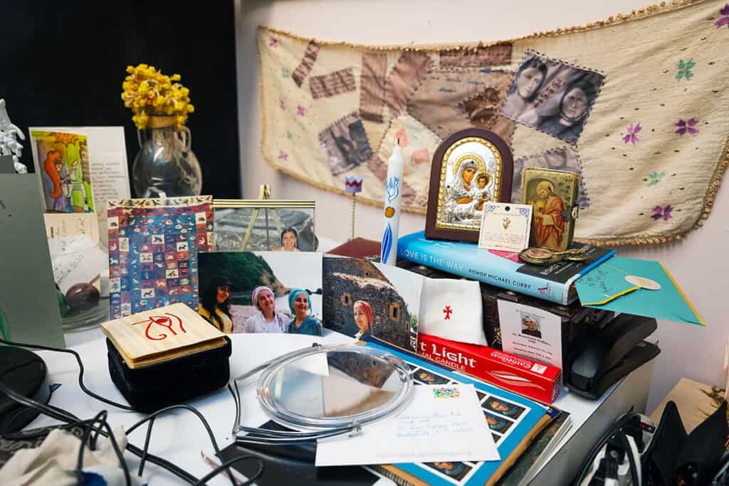 A studio display with embroidered family photographs, icons, flowers, books, and personal keepsakes.