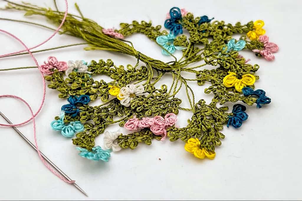 A close-up of colorful Oya lace flowers being made with thread and a needle.