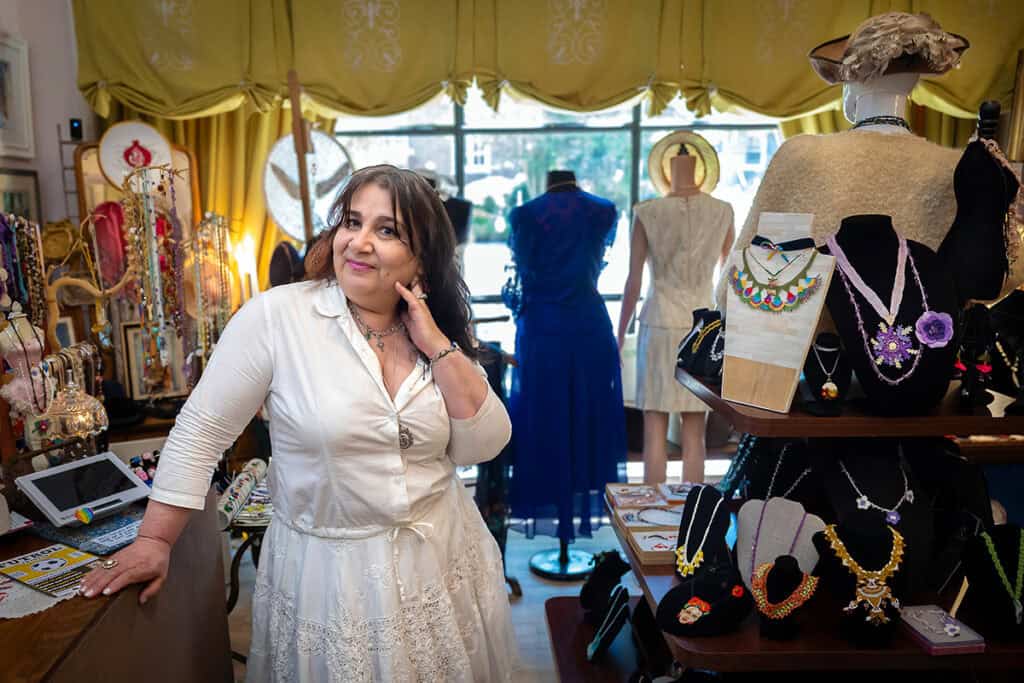 Ylvia Asal poses inside her Haddonfield studio among jewelry displays, garments, and textile artwork.
