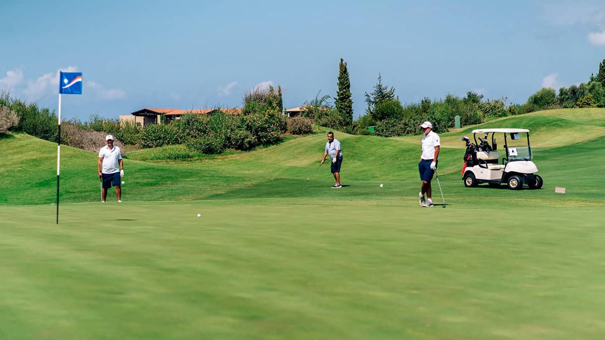Three golfers stand on a putting green beside a golf cart at Costa Navarino in Messinia, Greece.