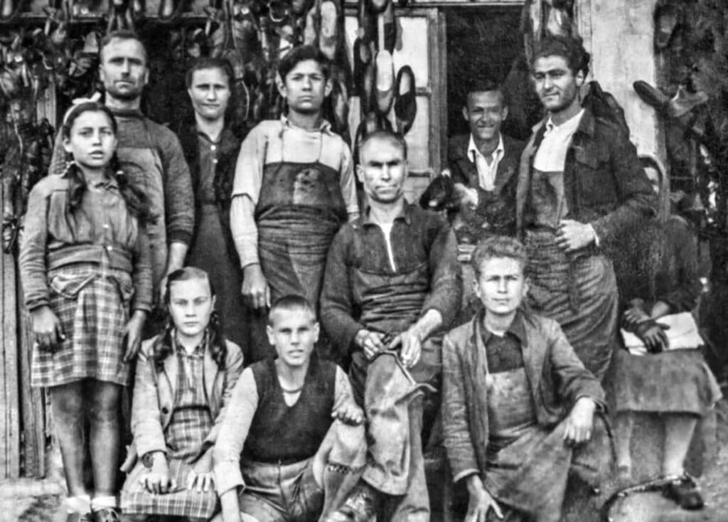 Shoemakers, family members and children gathered outside a workshop in Ossa