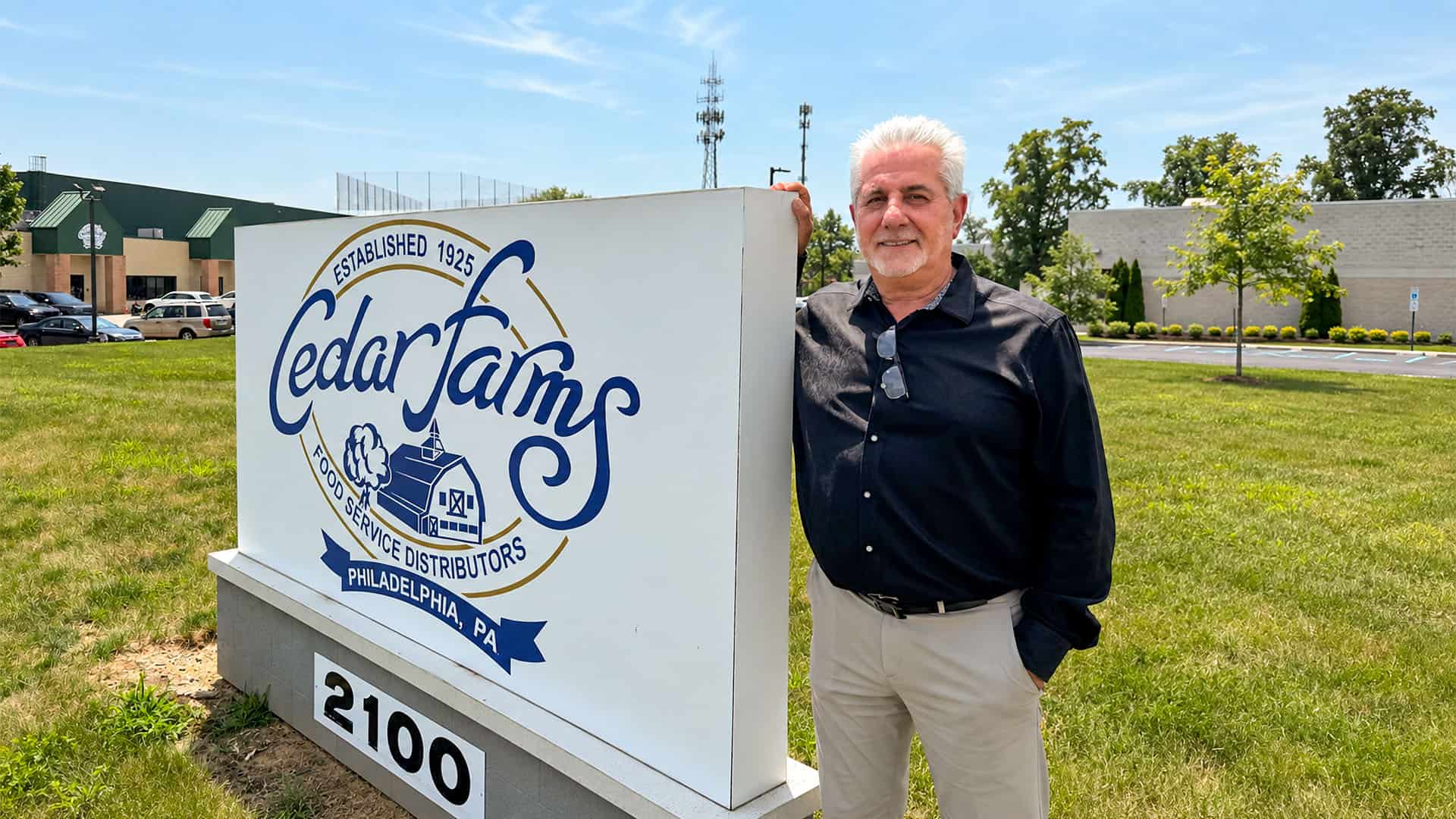Pete Pahides standing beside the Cedar Farms Food Service Distributors sign in Philadelphia.