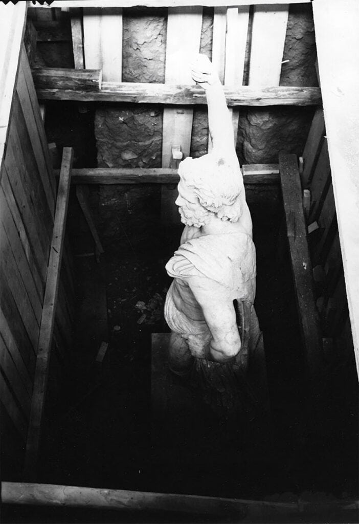 Ancient marble statue of Poseidon from Melos standing in a timber-lined concealment pit.