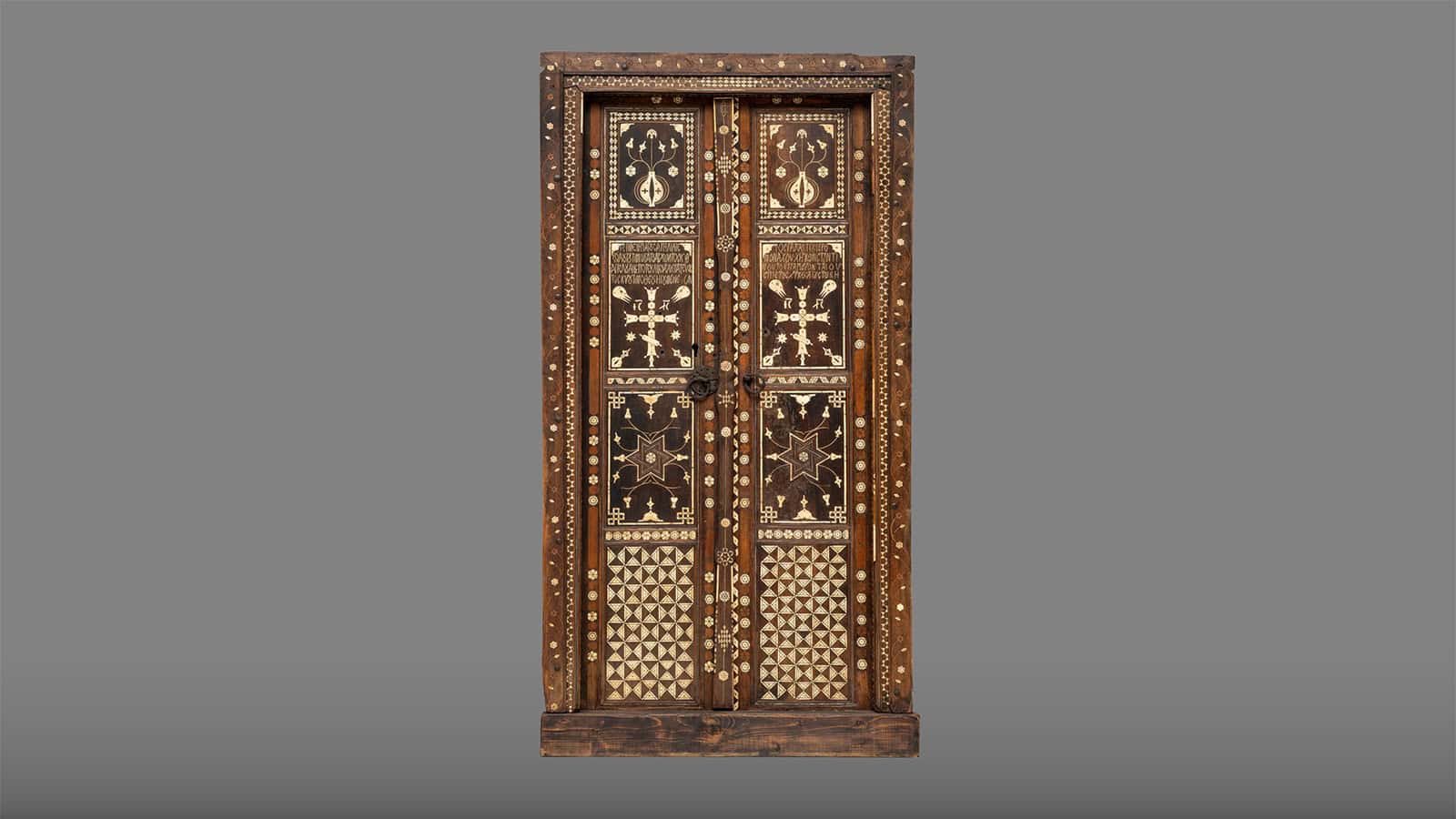 Historic double wooden church door with intricate geometric, floral, and cross-shaped inlays.