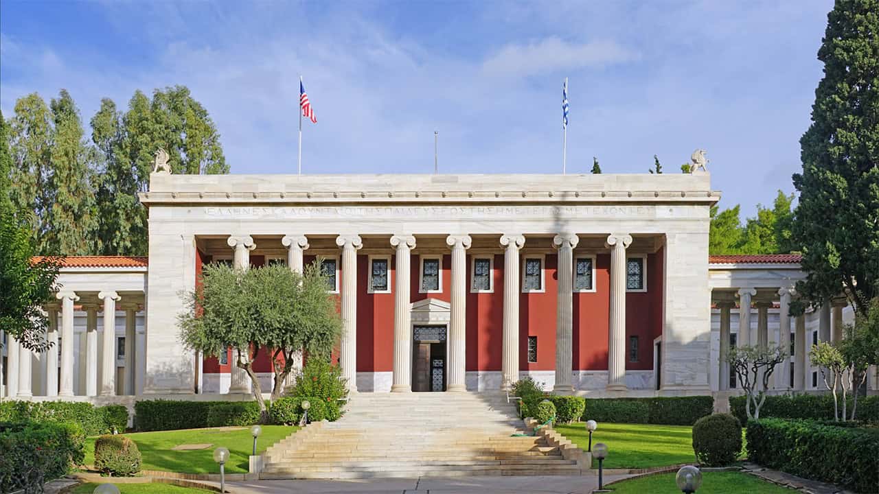 Exterior of the Gennadius Library in Athens, with its marble columns and Greek and American flags.