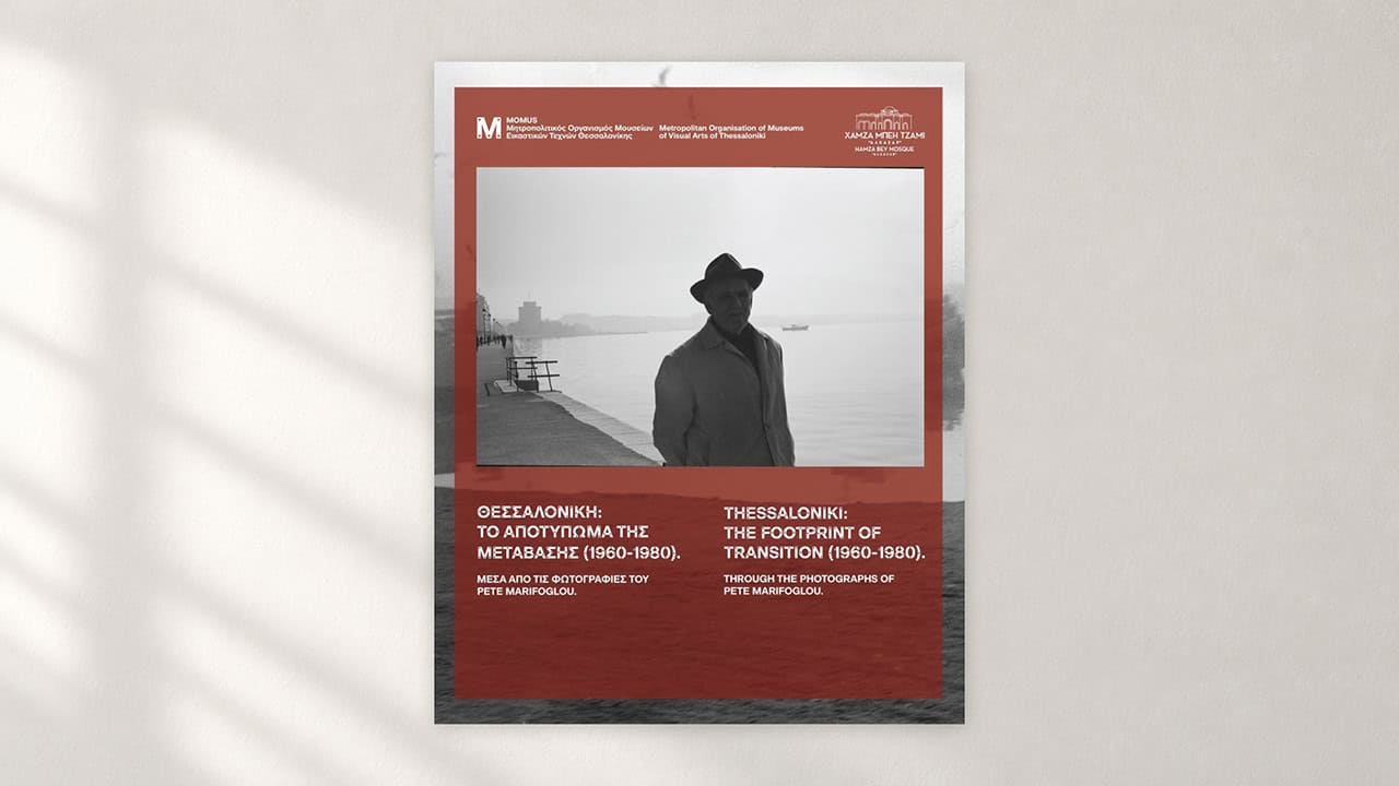 Official MOMus exhibition poster featuring a black-and-white photograph of a man standing along Thessaloniki’s waterfront, displayed against a neutral background.