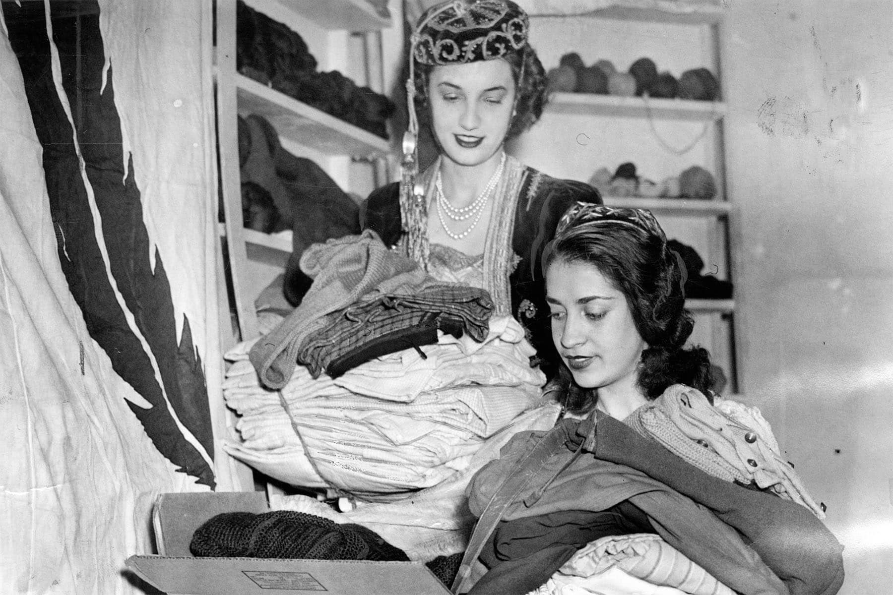 Christine Halkies and Niobe Stephano pack donated clothing into a large cardboard box, surrounded by stacks of garments at a Philadelphia Greek War Relief office.