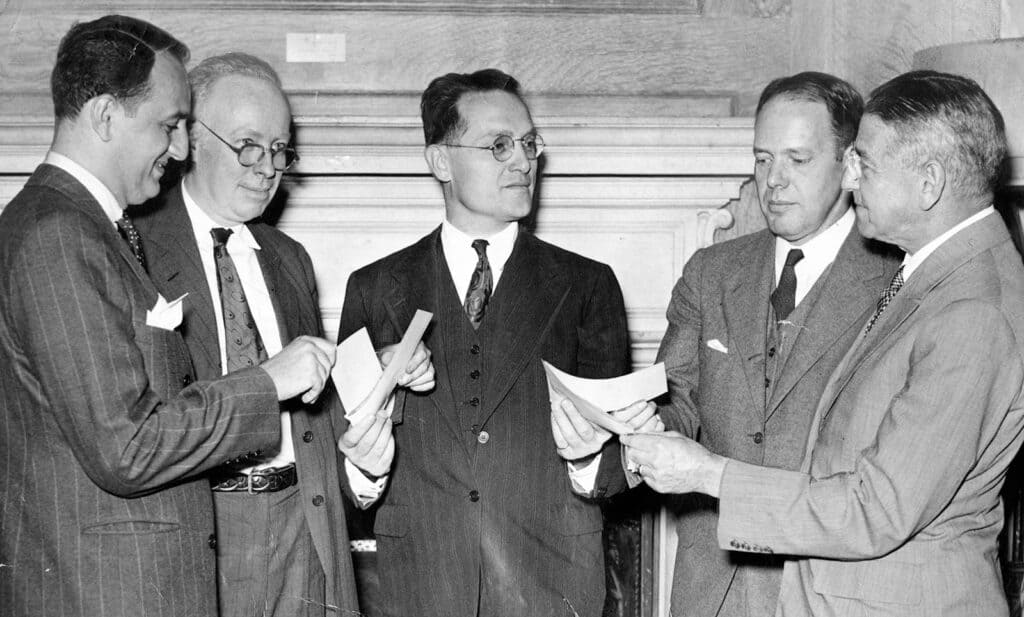 Five men in suits stand together examining checks during a wartime relief donation presentation at the Philadelphia Art Alliance.