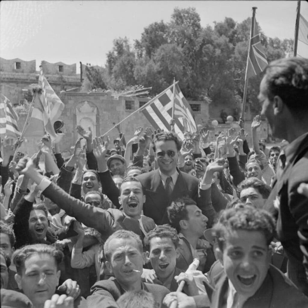 Jubilant crowds waving Greek, British, and American flags welcome Allied troops to Rhodes in May 1945.