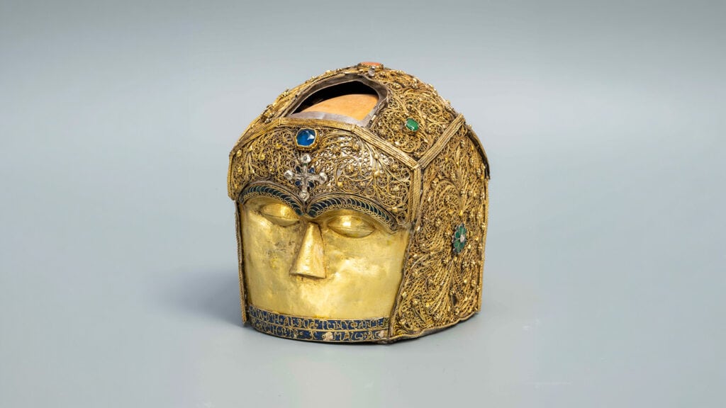 Gold-colored head-shaped reliquary of Saint Matrona, decorated with intricate filigree and colored stones.